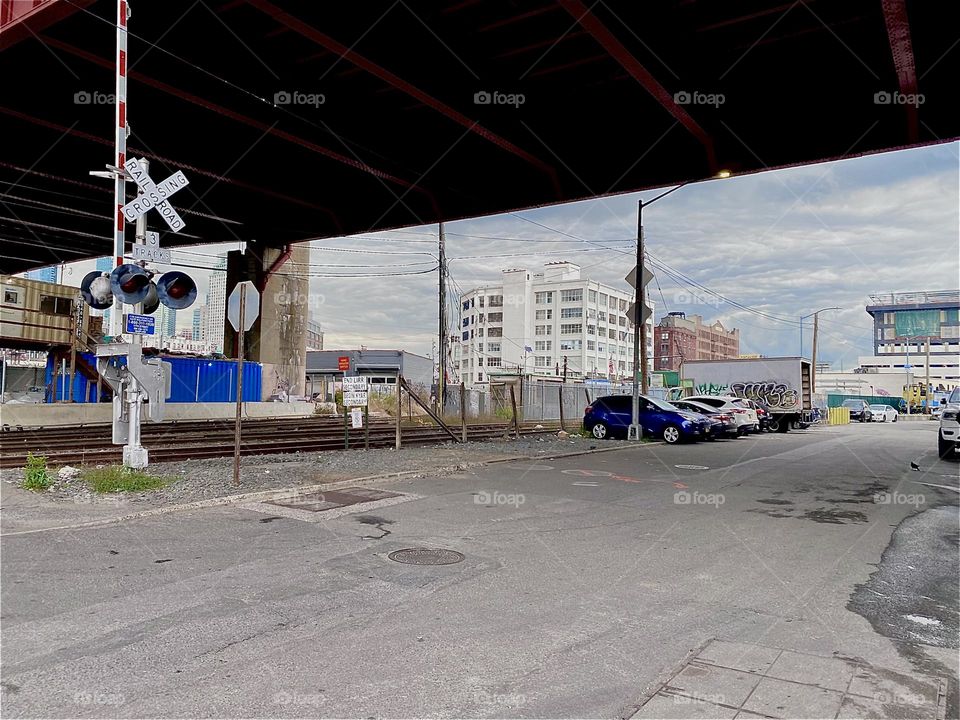 This is the parking lot underneath the “Pulaski Bridge” at “Newtown Creek” in LIC, Queens. The “Long Island Railroad” passes through here and periodically blocks pedestrian traffic whenever a train is expected. 2023. Hypnotic Productions