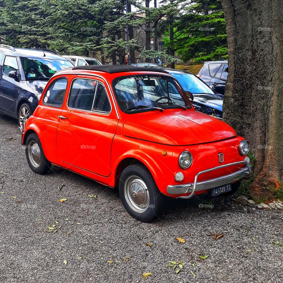 A small red car typical of Italy in the Italian city of Triest.