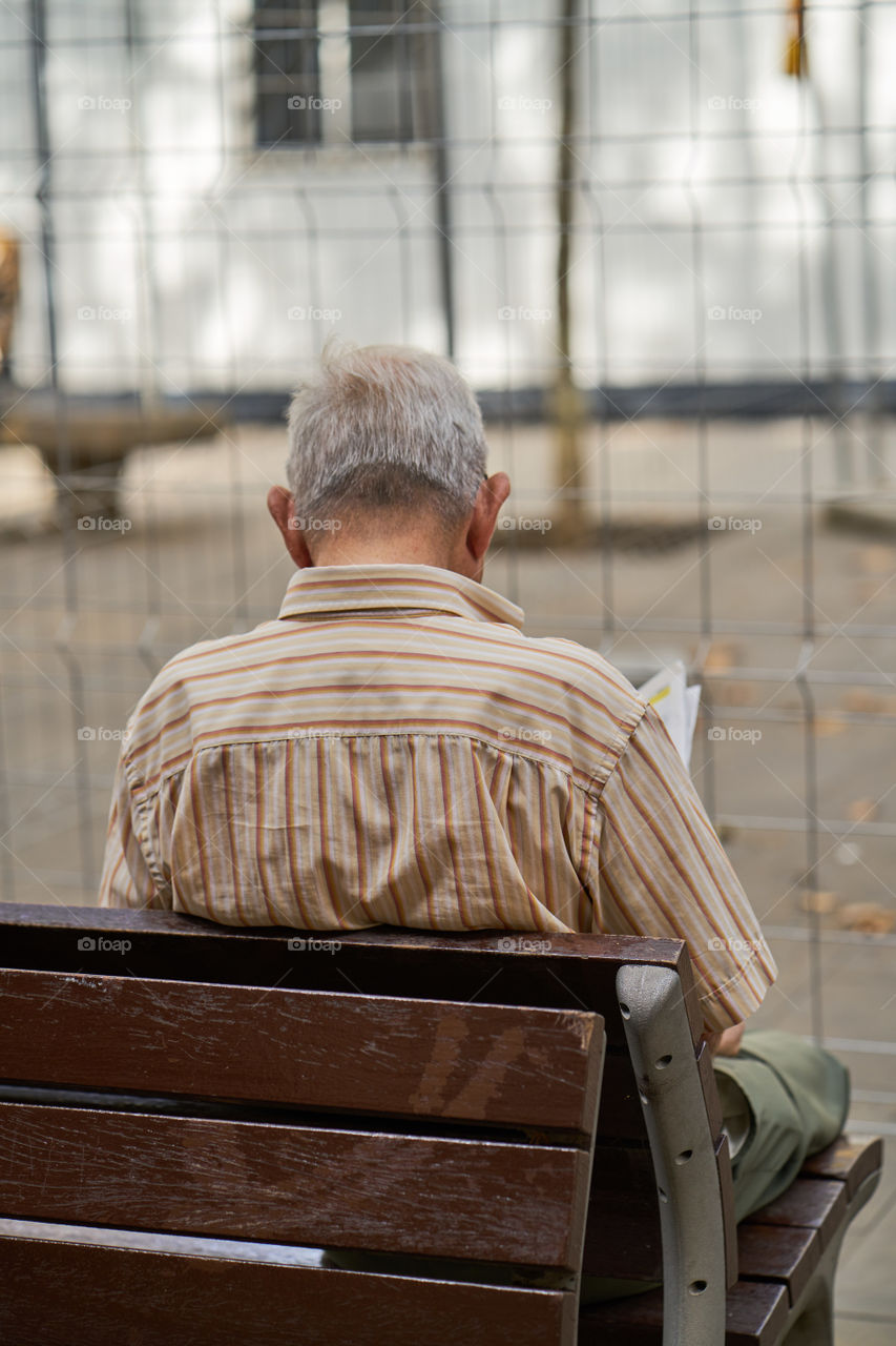 Elderly man reading the newspaper at a street bench