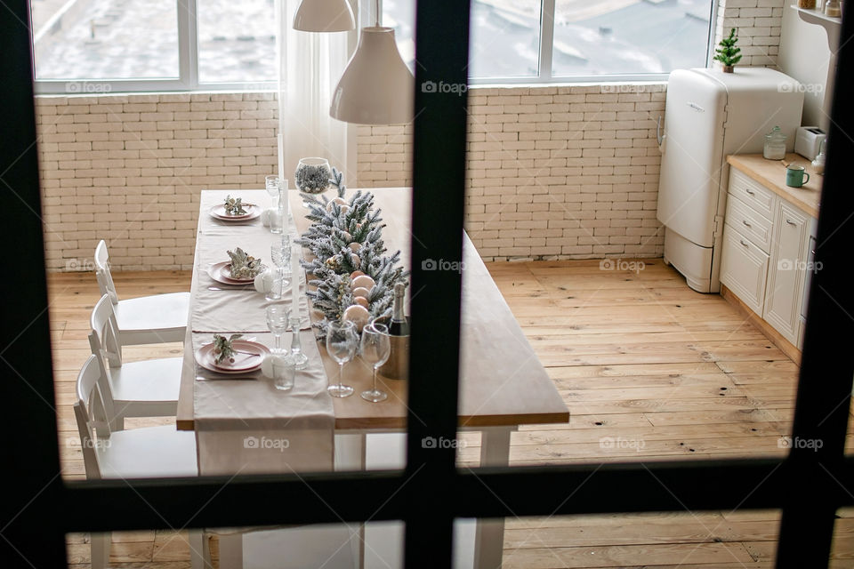 Festive winter cozy kitchen interior with garlands, decorations and gifts.  Christmas dinner at the decorated table.