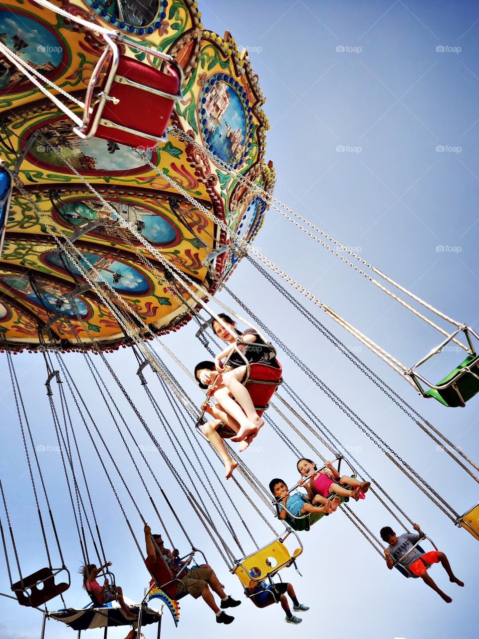 Children riding on colorful metal swings at a beach side amusement park on a sunny day. 