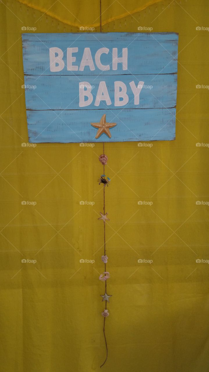 Blue "beach baby" sign on a yellow curtain