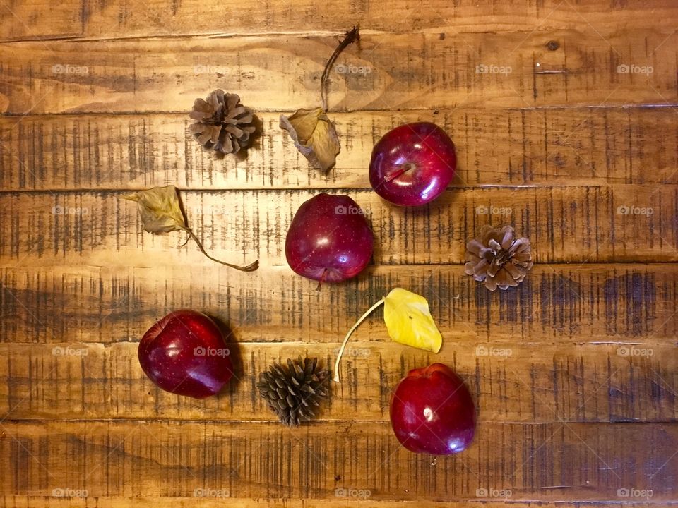 Red delicious apples, pine cones, and leaves with beautiful fall color on a pine wood table 