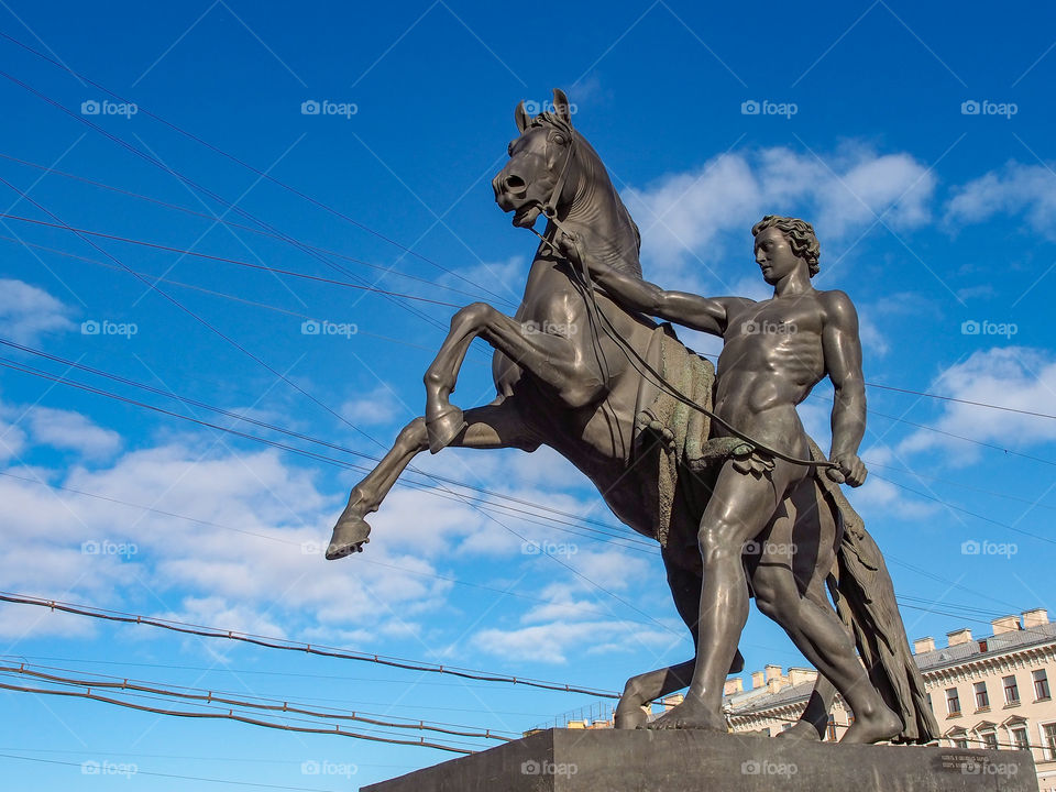 A bronze figure of a large size monument of a young man with a horse stands on a street of the city of St. Petersburg.