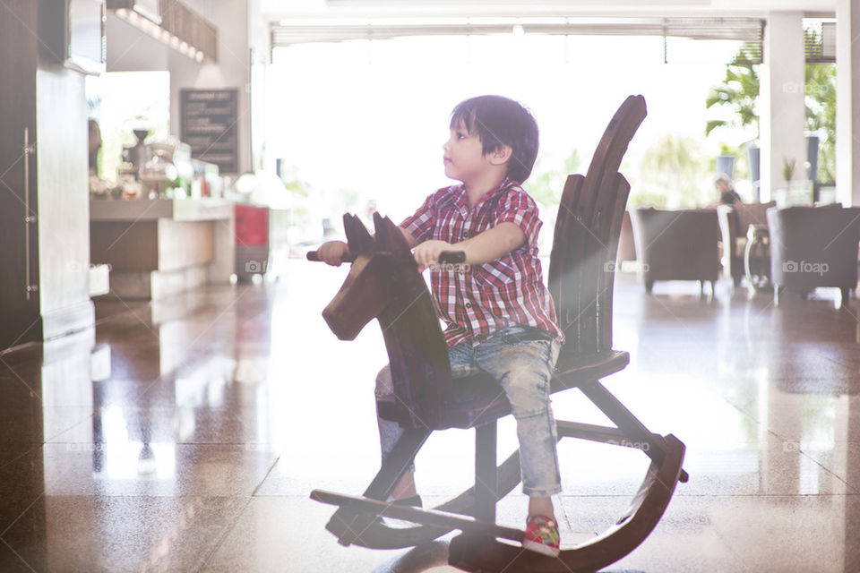 young Asian boy riding a wooden horse at hotel lobby. Thitiwin Dupont having fun 