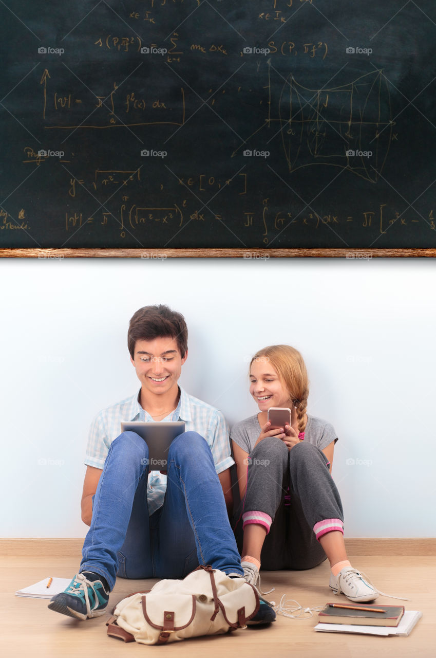 Girl and boy sitting on the floor under the blackboard in the classroom at school