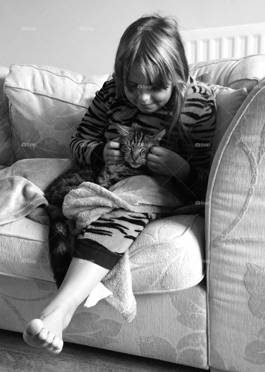 Little girl sitting on sofa with tabby cat