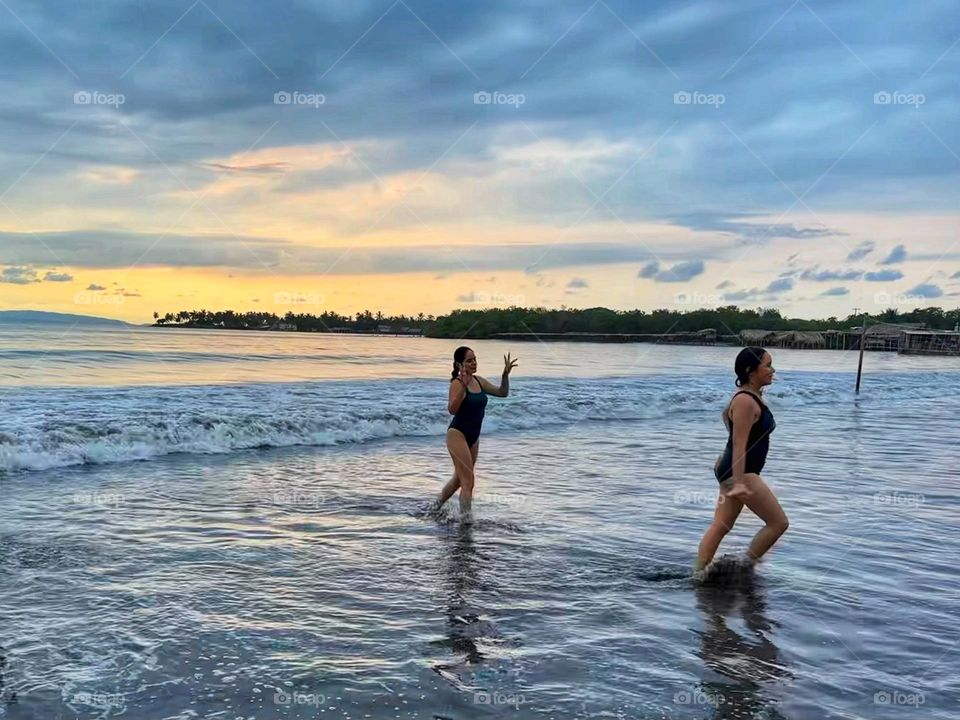 Sisters coming out of the ocean going to beachfront, enjoying the end of a sunset.