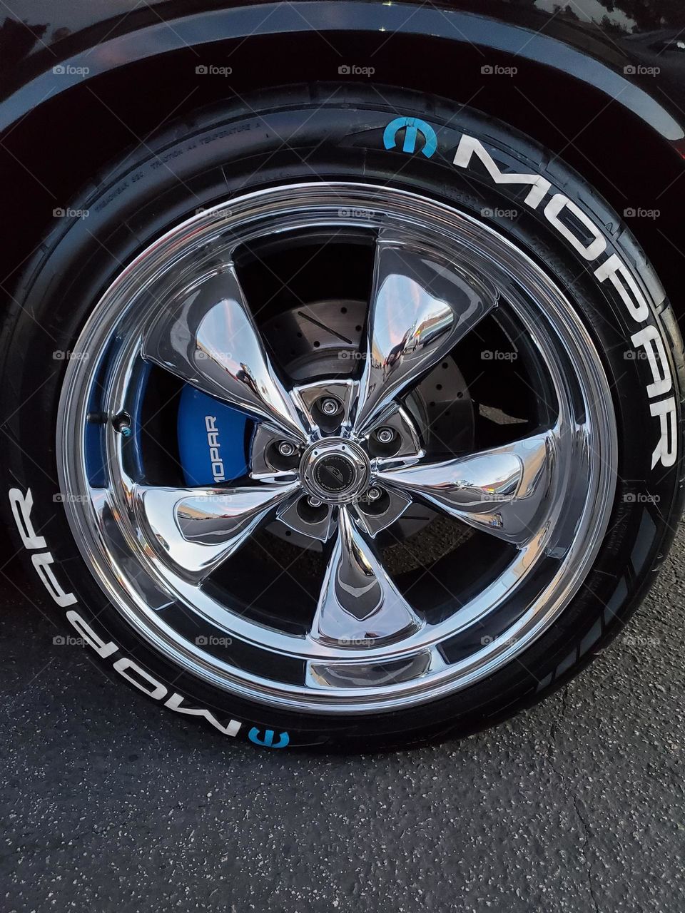 A classic chrome five spoke wheel is accented by a blue brake caliper and special tires