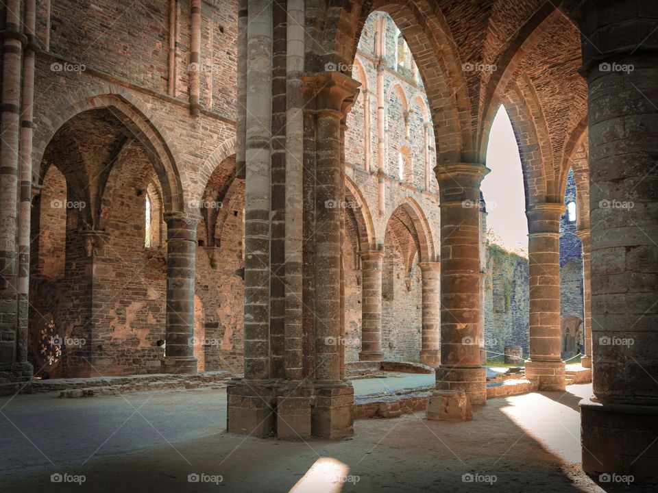 Ancient ruins with stone rhythmic columns and sand-colored arches in a medieval abbey in Belgium, close-up side view.