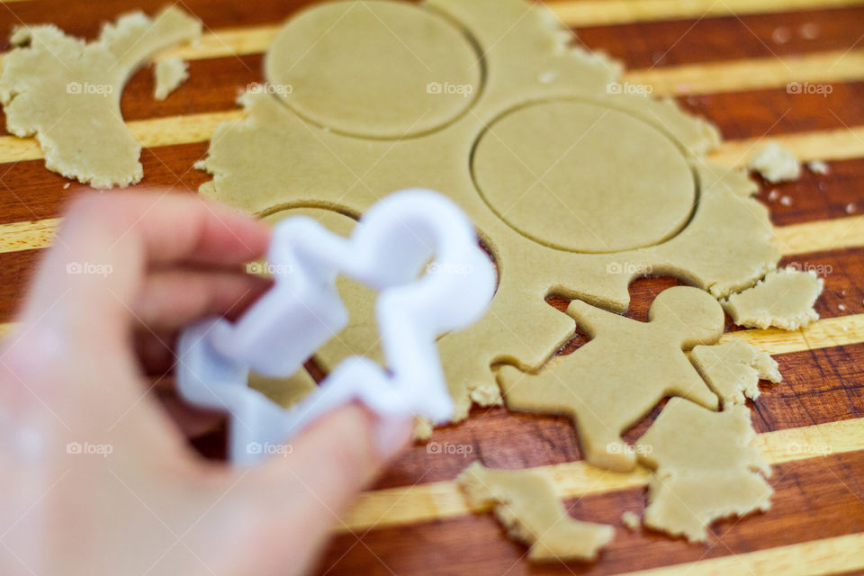 Cooking at home - making biscuits and cutting different shapes. Image of hand holding man shaped cookie cutter and homemade cookie dough and shapes.