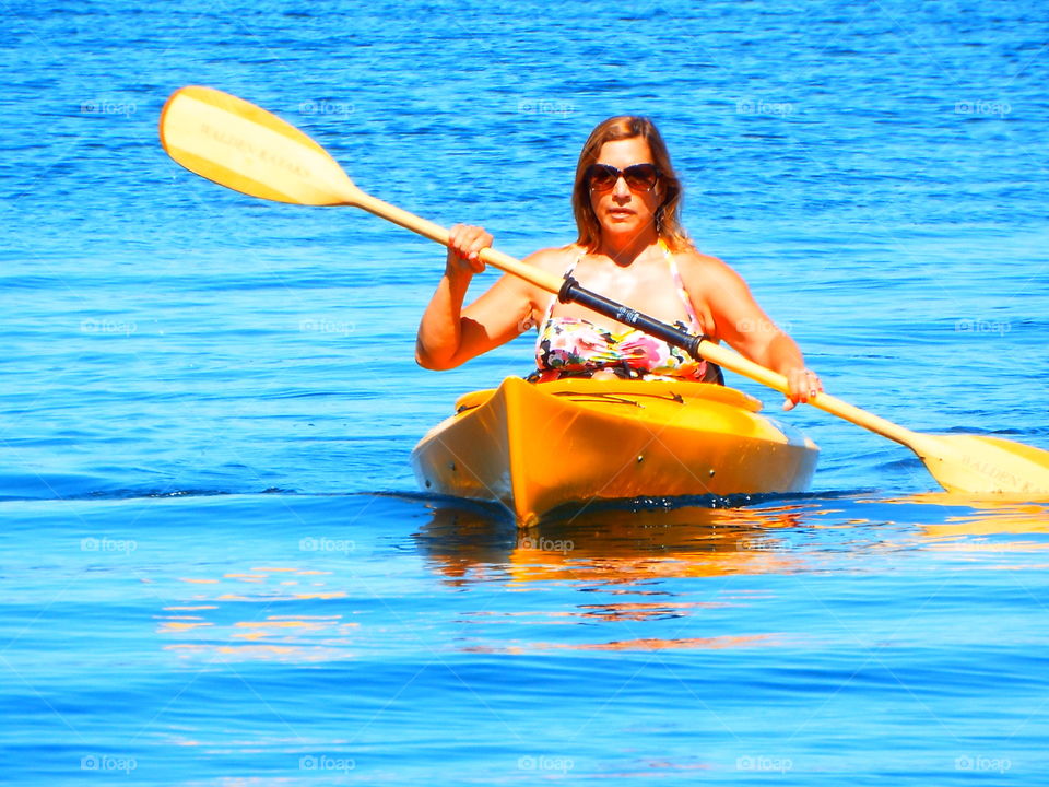 Woman in yellow kayak paddling in towards camera and beach