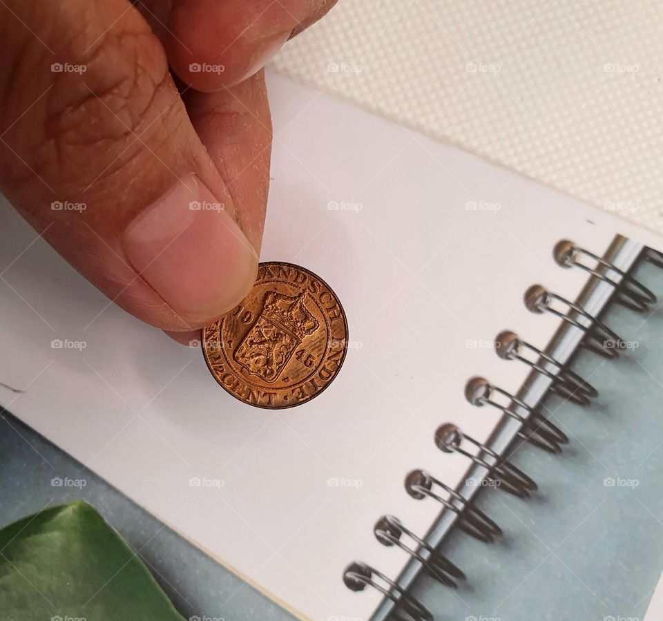 a human hand places a 1945 1/2 cent Netherland Indie coin on a block note on the desk