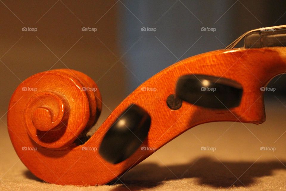 Violin laying on carpet tuning pegs and scrolling tip visible at floor level