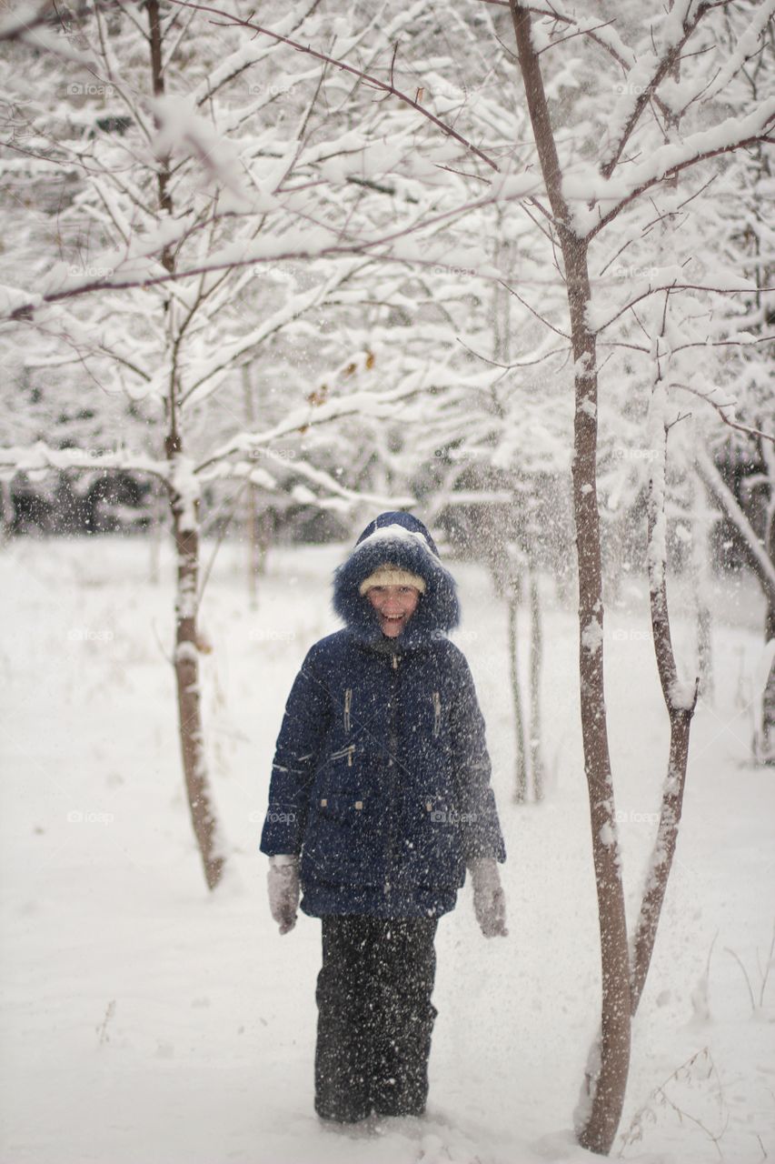 A girl stands under a tree from which snow is falling