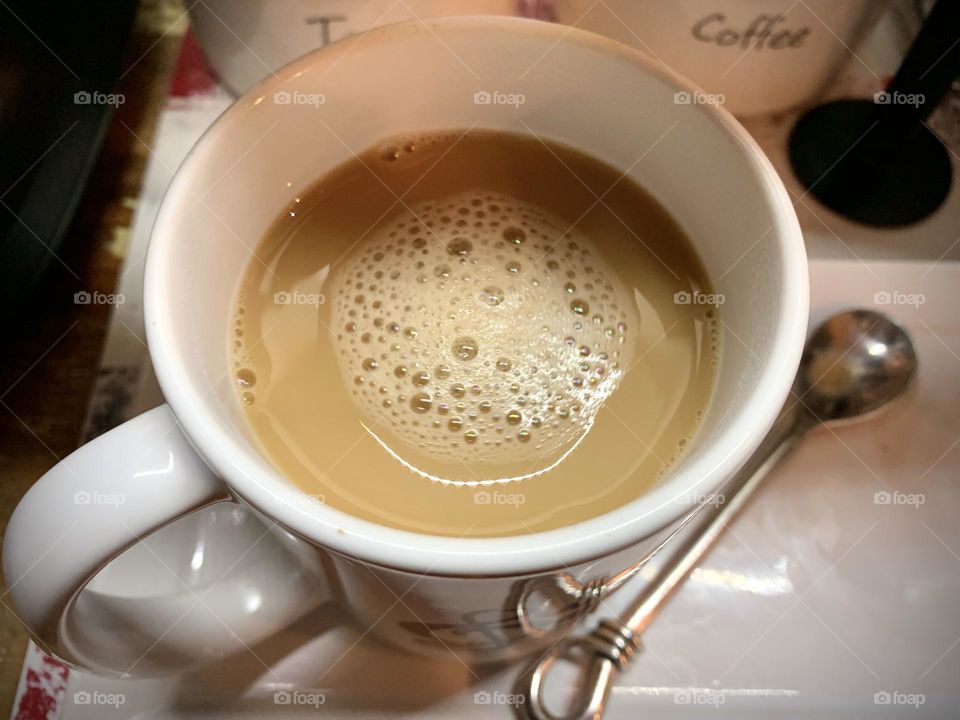 A morning cup of coffee to get the day started right. A home brewed cup of Joe, bubbles, and a silver spoon.