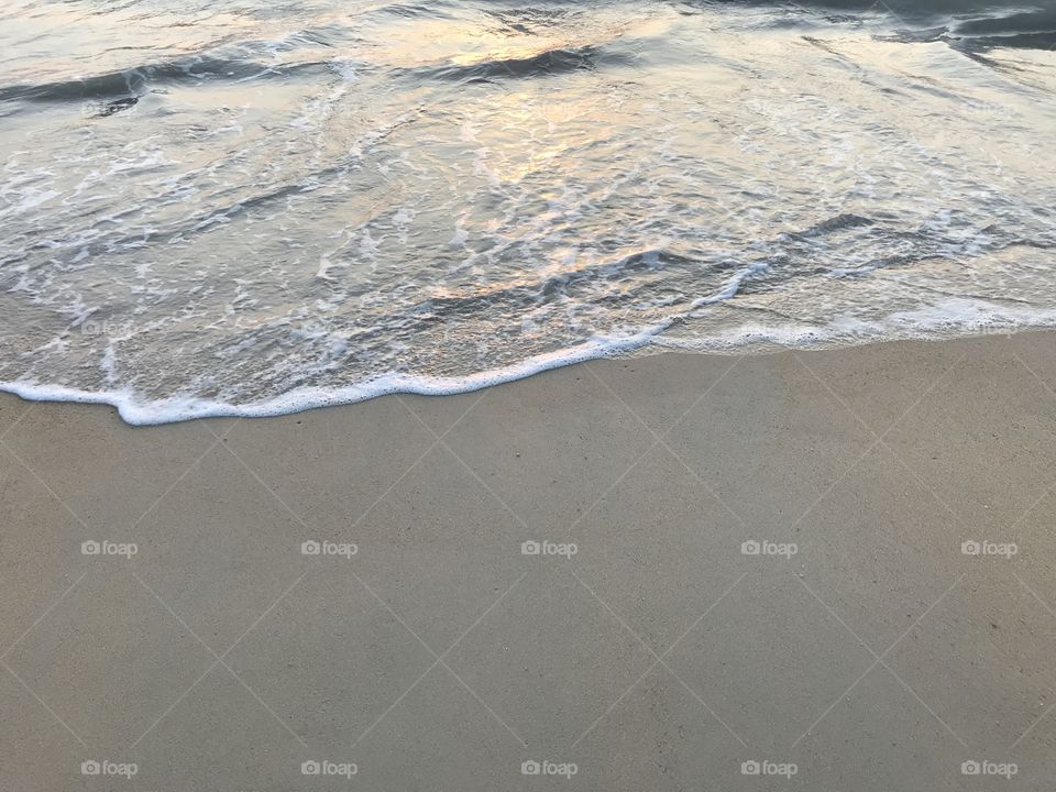 sea wave on the clear sand beach with sunset light shines above it