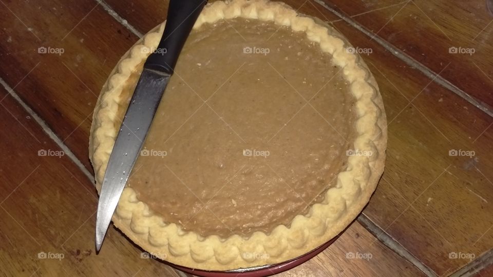 Pumpkin pie and a knife on a wooden table.