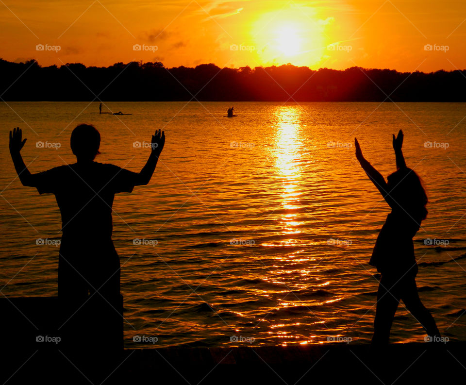 Waving in a distance . These 2 young, silhouetted children wave to their parents who are boating in the bay soaking up the magnificent sunset!