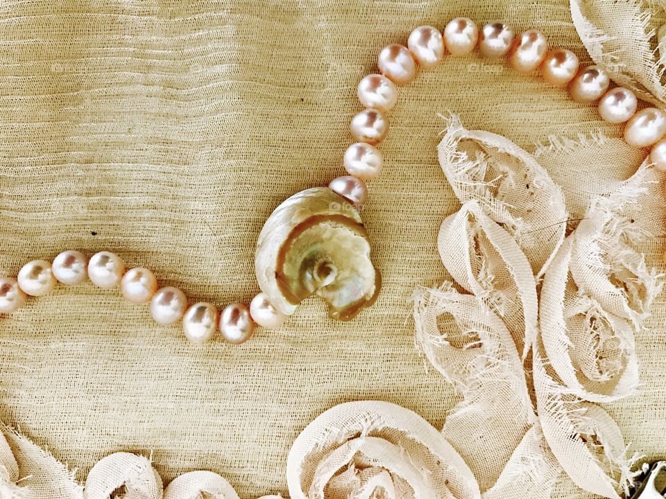 Pink pearl necklace with seashell on shawl of fabric roses