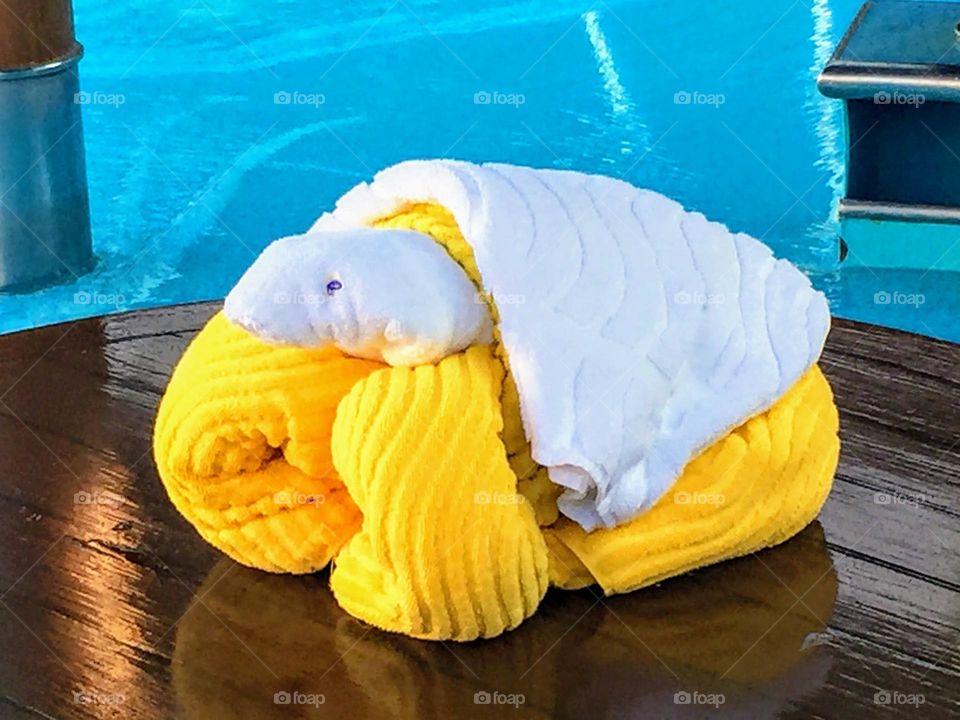 Yellow challenge towel art yellow and white elefant at the edge of the swimming pool with clear blue water 