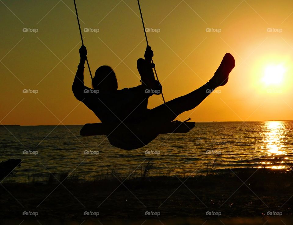 Silhouettes and shadows - A girl with a lot of energy swings high in the air over the bay while admiring the brilliant sunset. 