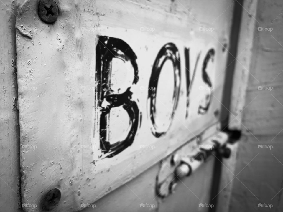 Black and white photo, rusty old door with old painted tin sign which reads BOYS. Old outside toilet, outside John, outside loo, men's room, boys room, 