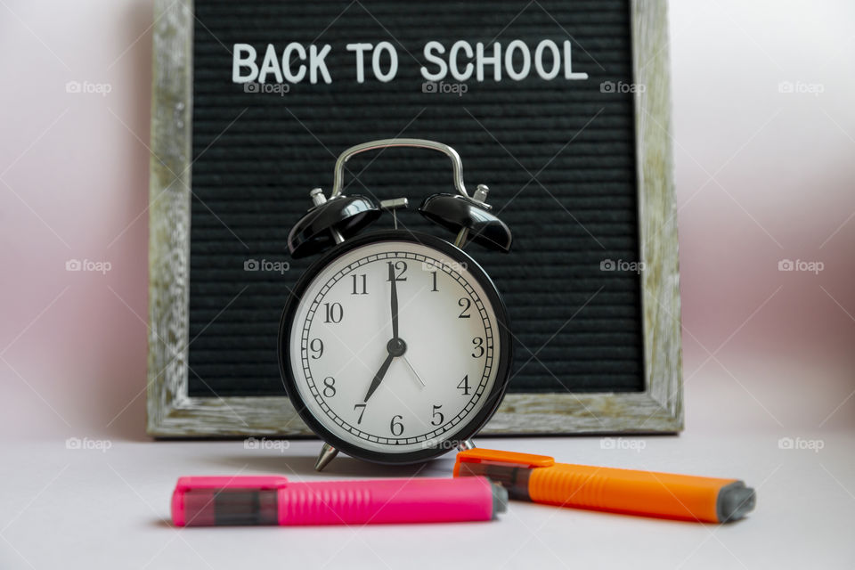 Felt board with the text Back to school with alarm set to 7am and colorful markers on pastel pink background