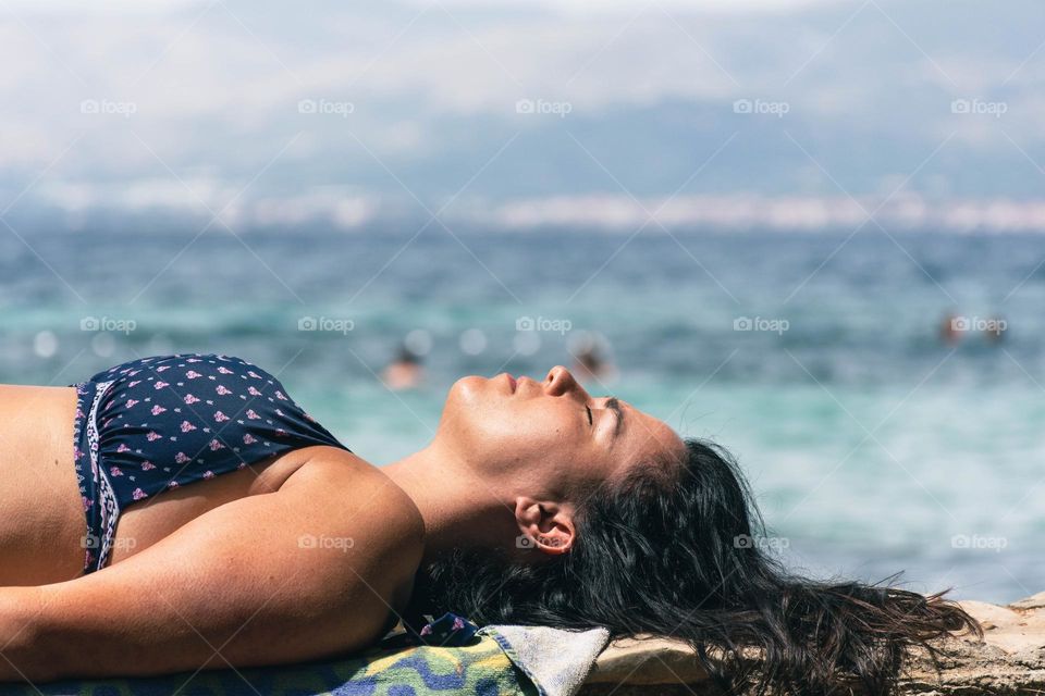 Side view of young woman in bikini sunbathing and relaxing on beach