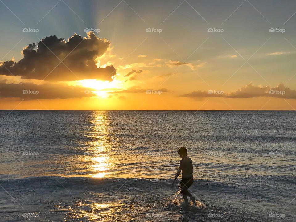 Fantastic cloudscape and sunset shine brightly on a child in the ocean.
