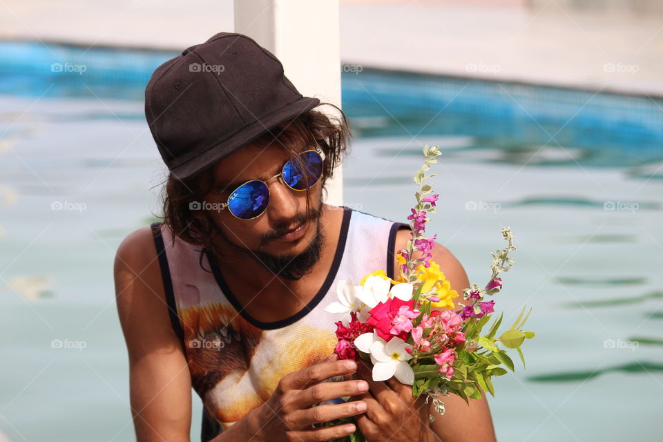 Young man holding flower bouquet and sitting at poolside