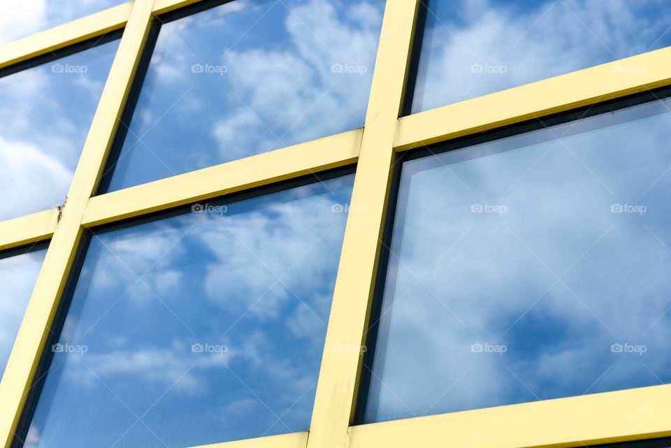 Close-up of yellow square windows outdoors with the reflection of blue sky and white fluffy clouds