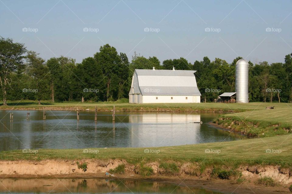 Farm landscape of a barn and silo by a pond.