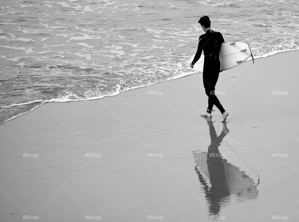 A surfer enters the water as he casts a reflection.