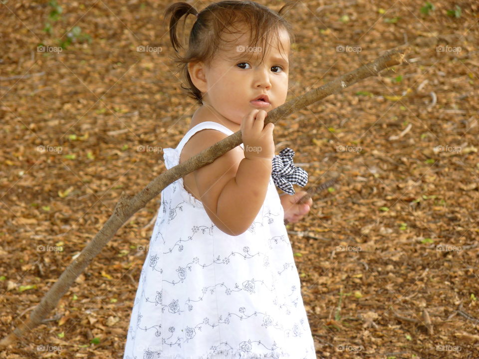 Child walking on leaves under tree with stick