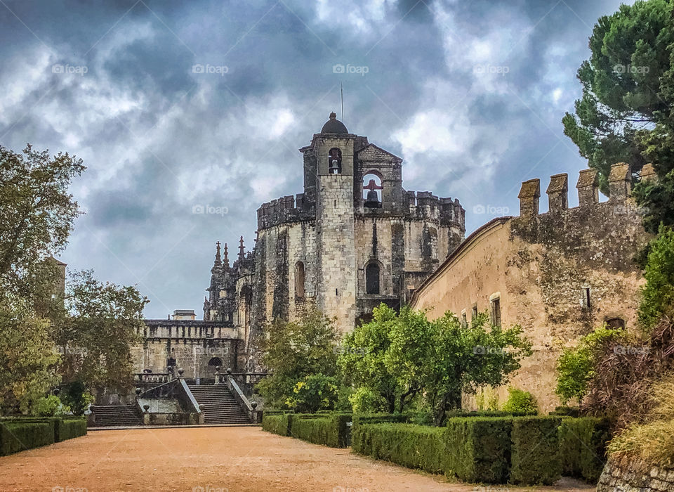 A long drive with manicured hedges leads up to the Convent of Christ on a cloudy day in Tomar, Portugal 