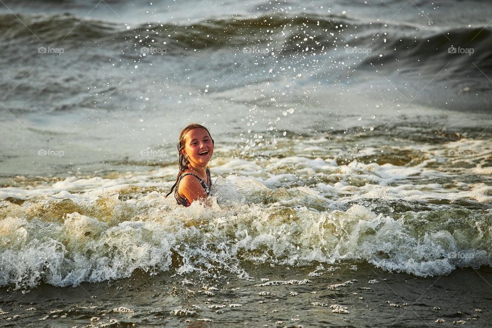 Little girl playing with waves in the sea. Kid playfully splashing in waves. Child jumping in sea. Vacations on the beach. Water splashes. Fun and play during summer vacation. Travel concept