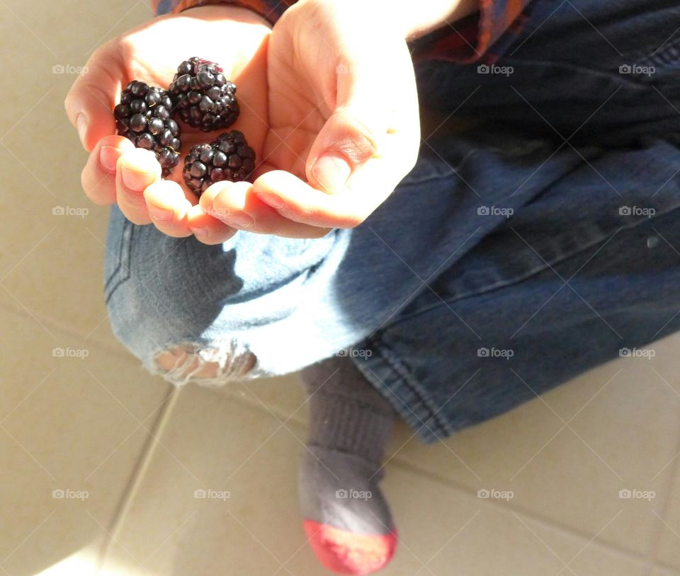 child holding blackberries over ripped jeans