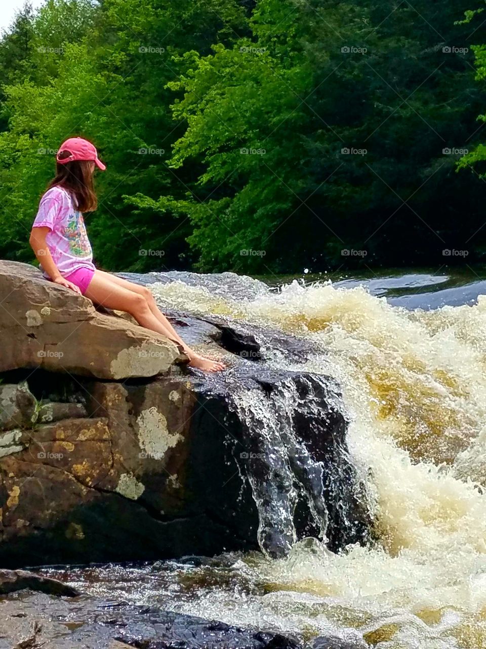 girl sitting on rocks on edge of splashing waterfall