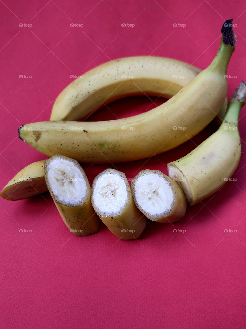 two whole bananas One banana is cut into pieces.  Red background