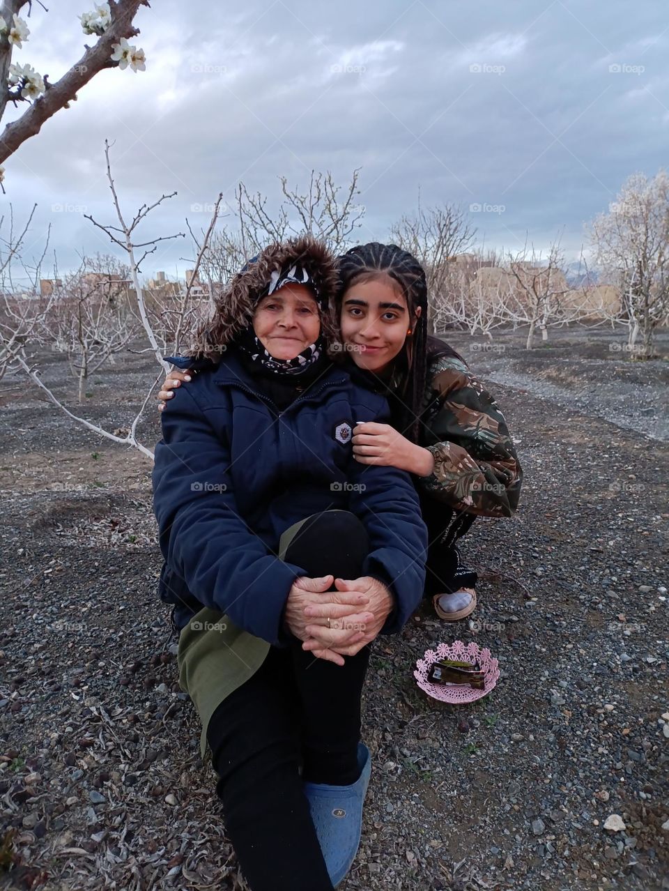 A picture of an old and tired mother with a smiling face next to her grandson who can see all her love for her grandson in her eyes.