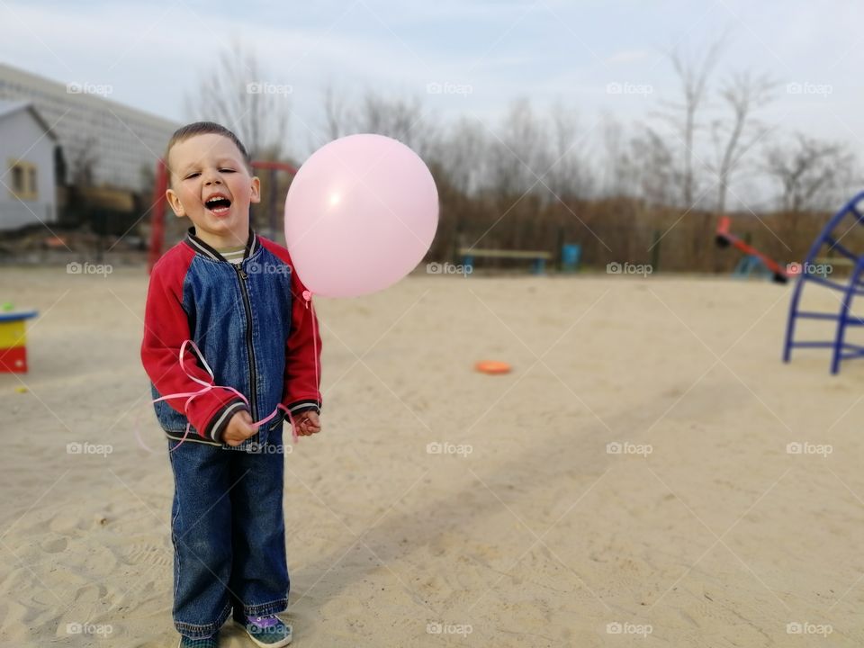 Boy in jeans smiles and screams, holds a pink air balloon