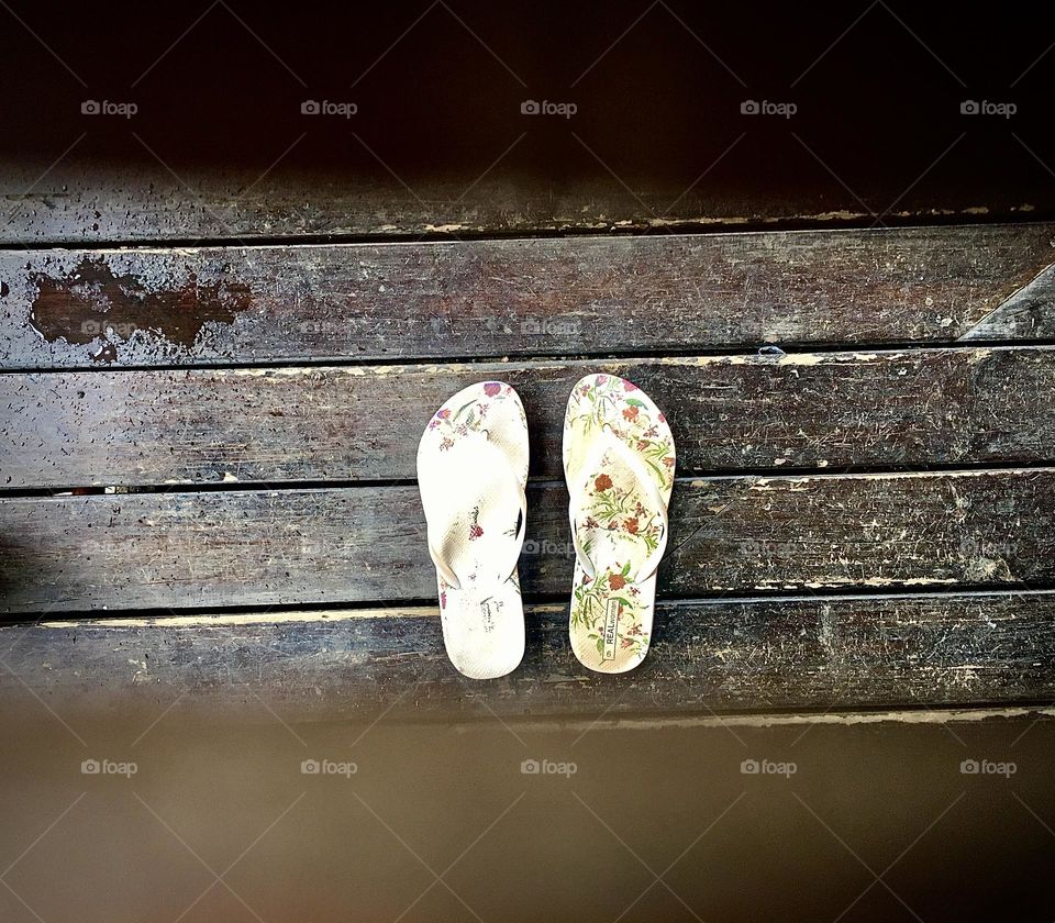 Beach sandals seen through the opening of a wooden table. 