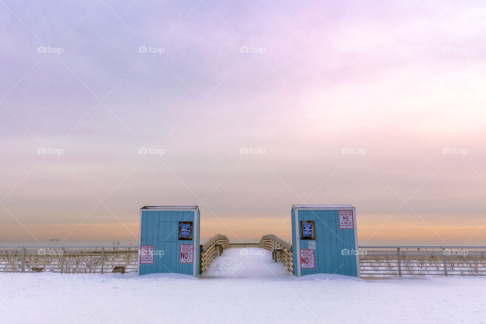 Two wooden booths at the entrance to a beach, under soft pastel sunset colors. 