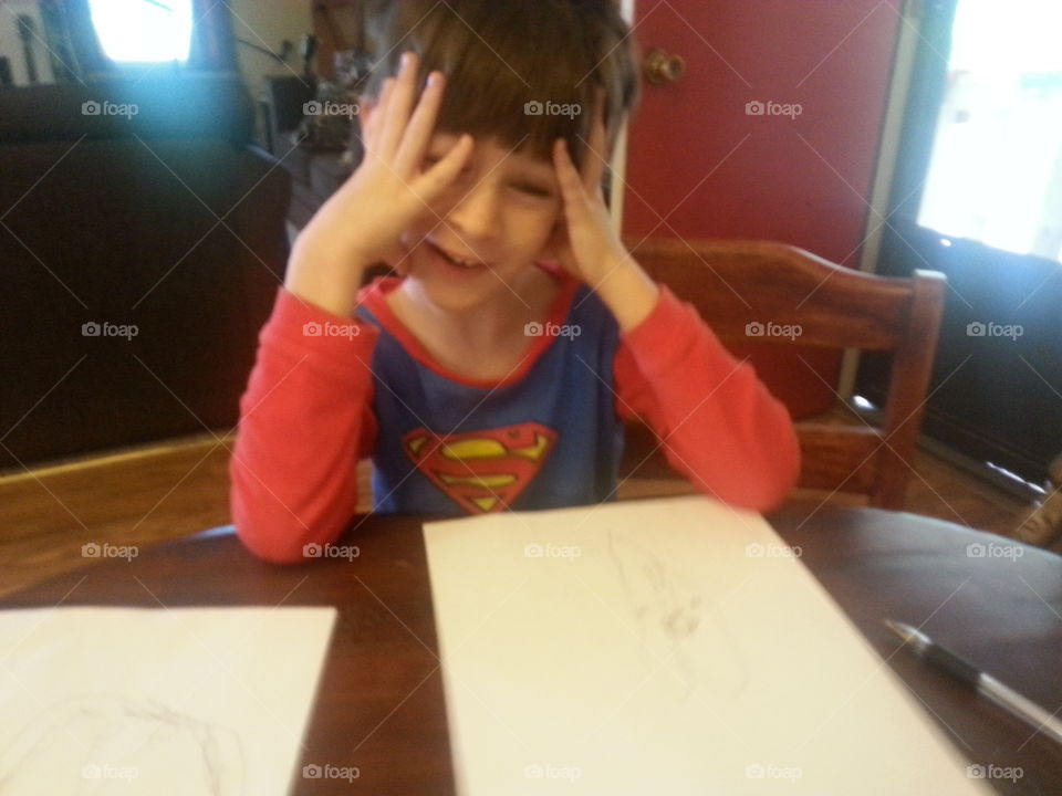 Cute little  boy sitting at the table in his pajamas with some paper about to write a story. 