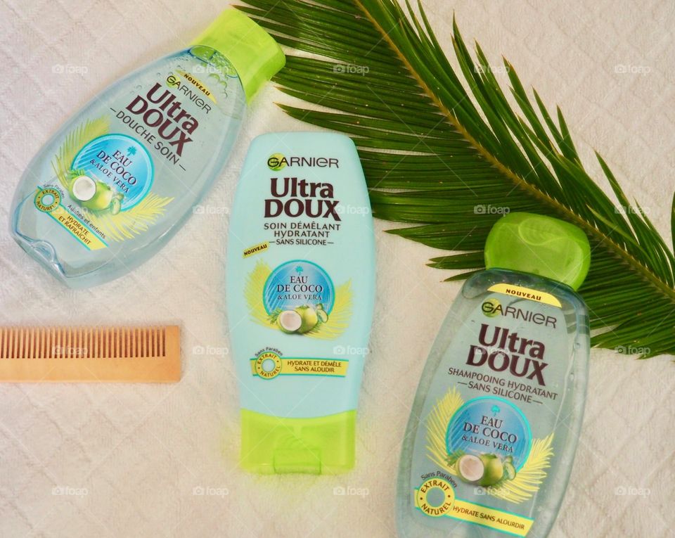 Garnier shampoo, conditioner and bath gel on a white towel with comb and palm leaf.