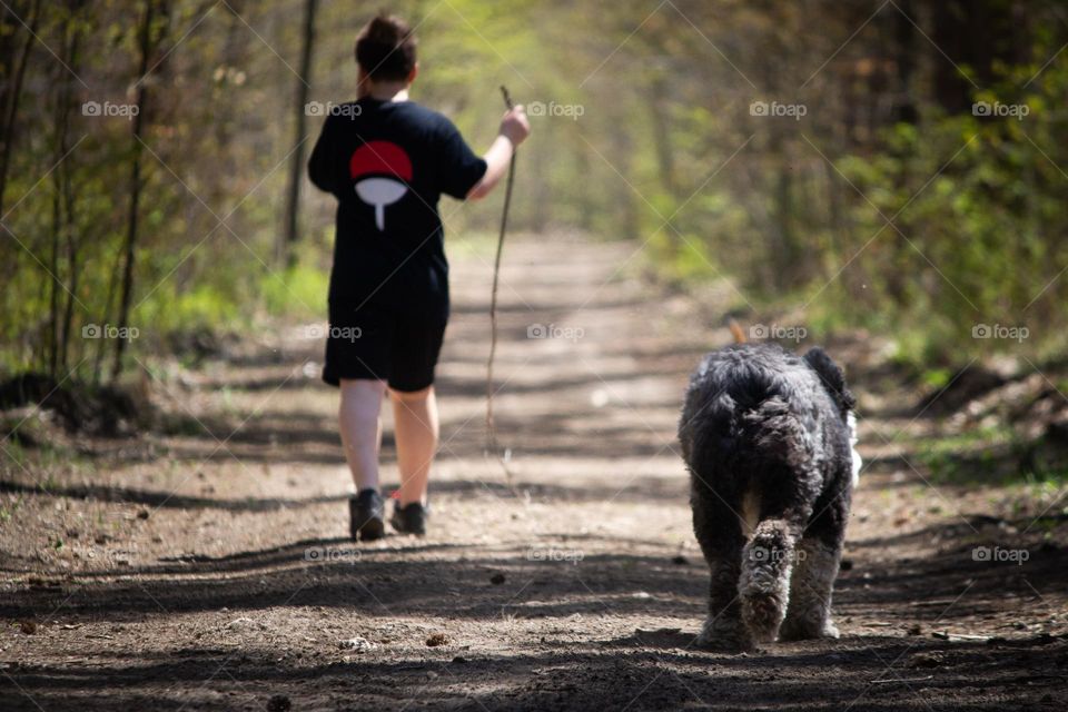 Person wearing black shirt and shorts taking the dog for a walk in the woods on a trail.