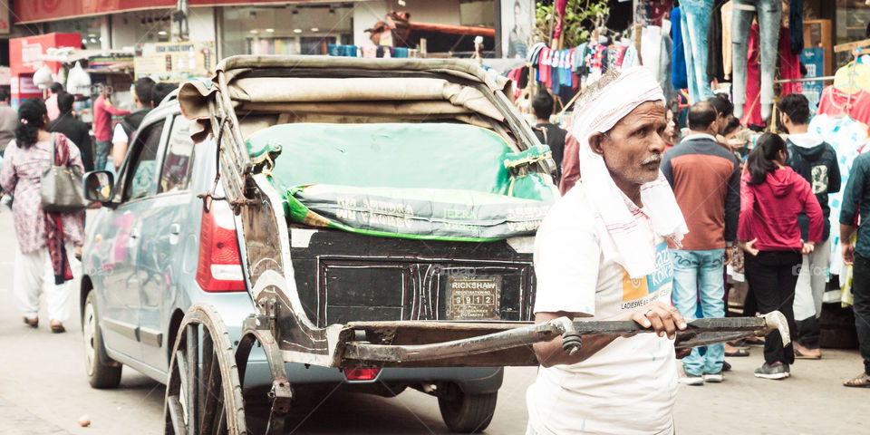 KOLKATA, WEST BENGAL, INDIA - JANUARY 5 2019: A Rickshaw puller carrying a rickshaw also called " tana rickshaw" in busy Kolkata Street. A human powered transport a runner draws a two-wheeled cart