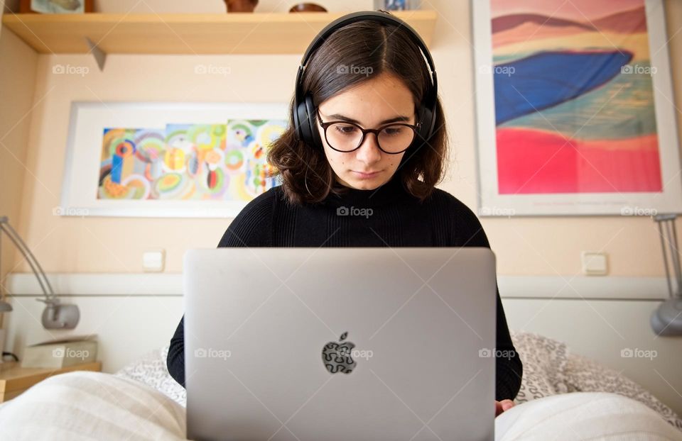 Teenage student with her laptop sitting on the bed