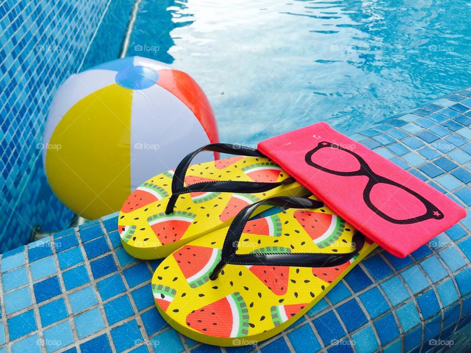 Flip flops with watermelons,pink sunglasses case and water ball near the pool